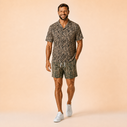Man wearing Silpaz tree bark camo mesh shorts in Green Leaf Camo with a matching camp shirt, full length front view