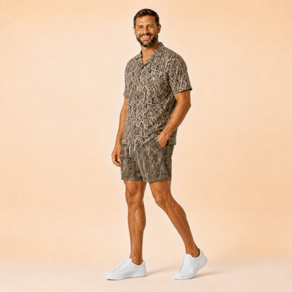 Man wearing Silpaz tree bark camo mesh shorts with a matching camp shirt, full length walking pose