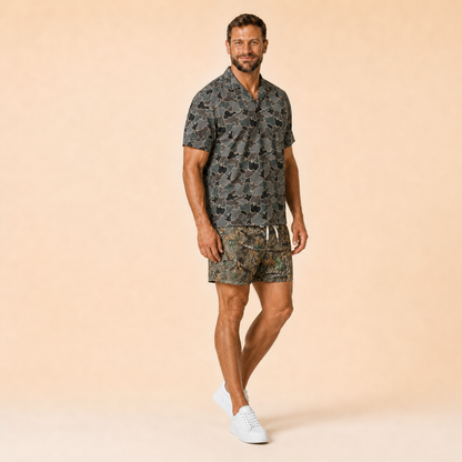 Man wearing Silpaz realistic camo mesh shorts with a dark camp shirt, full length view with a hand in his pocket