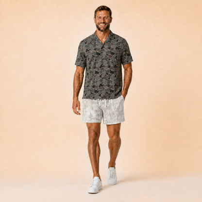 Man wearing Silpaz realistic camo mesh shorts in light snow camo with a dark camp shirt, full length front view