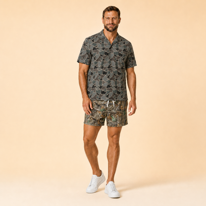 Man wearing Silpaz realistic camo mesh shorts with a dark camp shirt, full length three-quarter view