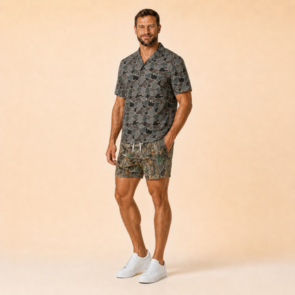 Man wearing Silpaz realistic camo mesh shorts in Brown Timber Camo with a dark camp shirt, full length front view