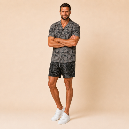 Man wearing Silpaz duck camo sport shorts in Black Camo with a dark camp shirt, full length front view